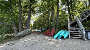 A sandy area with a wooden staircase, red chairs, and kayaks.