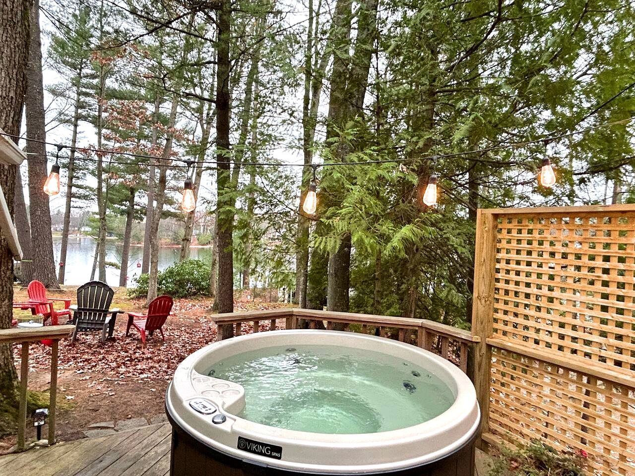 A hot tub surrounded by a wooden deck, chairs, and a wooden fence with a lattice design.