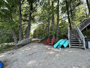 Ein sandiger Bereich mit einer Holztreppe, roten Stühlen und Kajaks.
