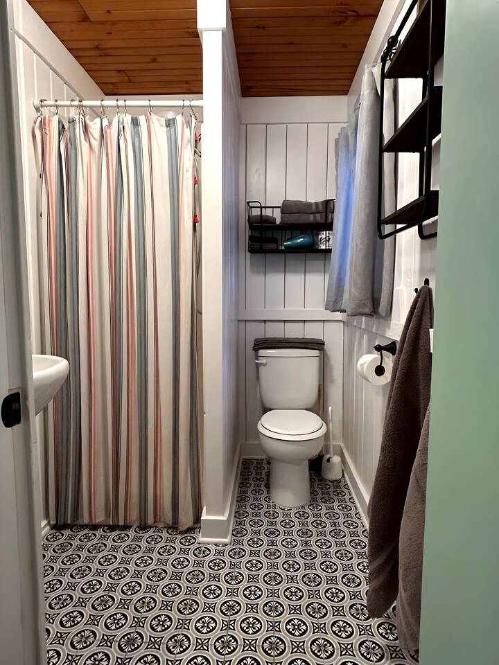 Een kleine, praktische badkamer met een gestreept douchegordijn, toilet, een plankje met handdoeken en vloertegels met een patroon.