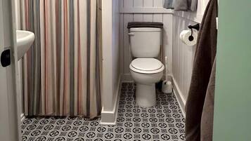 Een kleine, praktische badkamer met een gestreept douchegordijn, toilet, een plankje met handdoeken en vloertegels met een patroon.