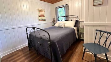 A bedroom with a bed, a chair, a window with curtains, a wall-mounted sign, and a wall decoration.