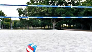 A volleyball on a sandy surface with a net in the background.