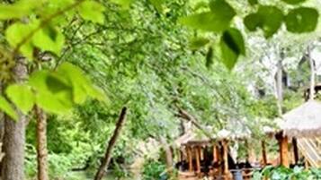 Une rivière où naviguent des bateaux, bordée d’une végétation luxuriante et entourée de huttes traditionnelles.