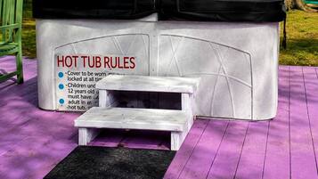 A hot tub with a covered top, a small step, and a sign listing hot tub rules.