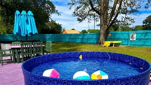 A round swimming pool with inflatable balls, surrounded by a fence and outdoor furniture.