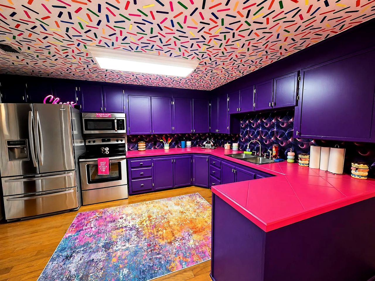 A modern kitchen with purple cabinets, stainless steel appliances, and a colorful abstract rug.