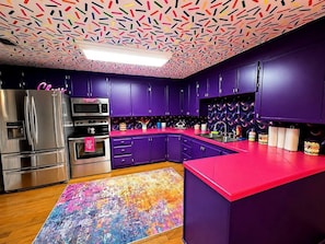 Eine moderne Küche mit violetten Schränken, Edelstahlgeräten und einem farbenfrohen abstraktem Teppich.