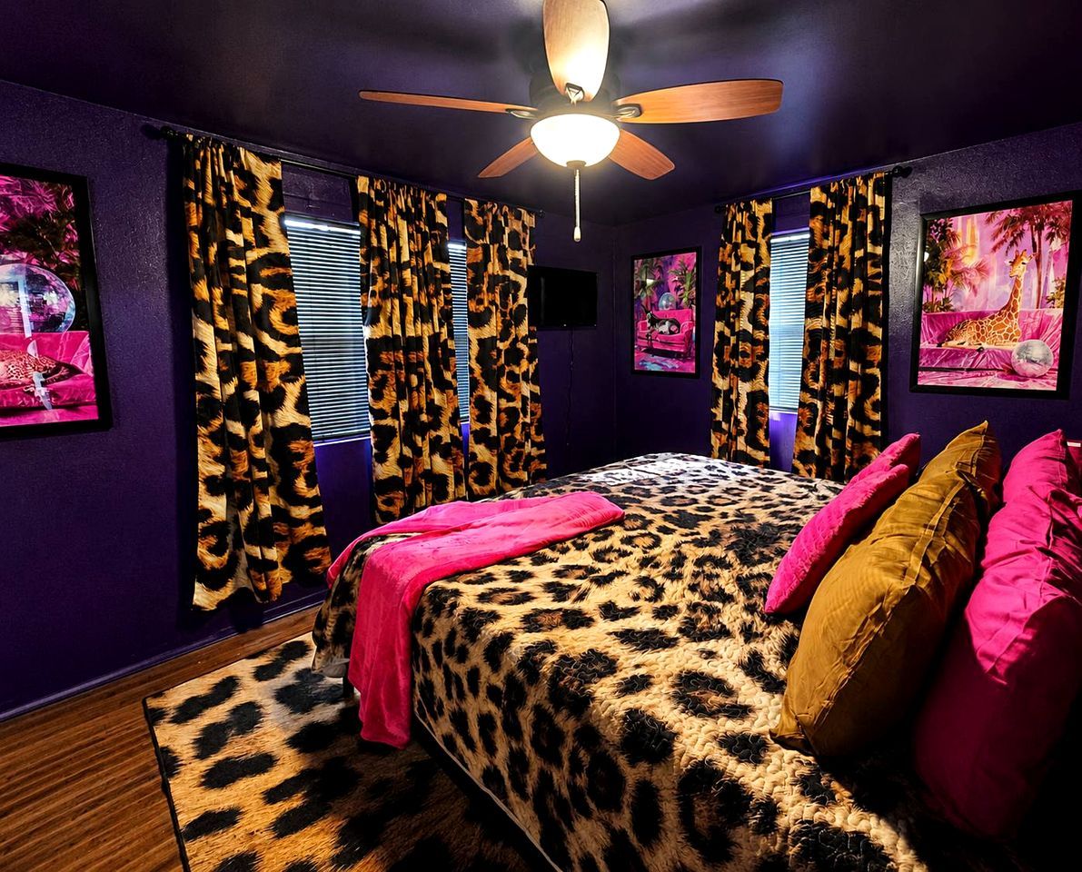 A bedroom with a leopard print bedspread, a ceiling fan, and curtains with a leopard print pattern.