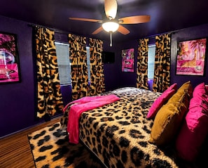 Un dormitorio con colcha de estampado de leopardo, ventilador de techo y cortinas con estampado de leopardo.