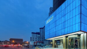 A modern hotel with a prominent glass facade, a traditional building in the background, and a busy street with moving vehicles.