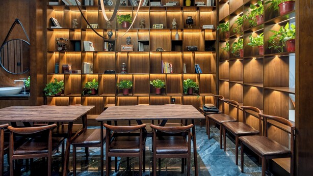 A modern interior with wooden panel walls, bookshelves, potted plants, and a marble floor.