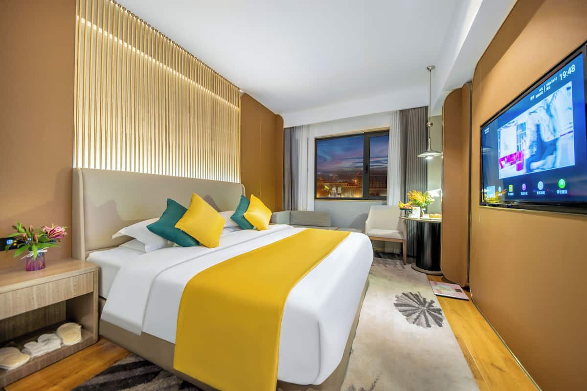 Habitación de hotel con una cama grande, televisión, escritorio y vista a la ciudad al anochecer.