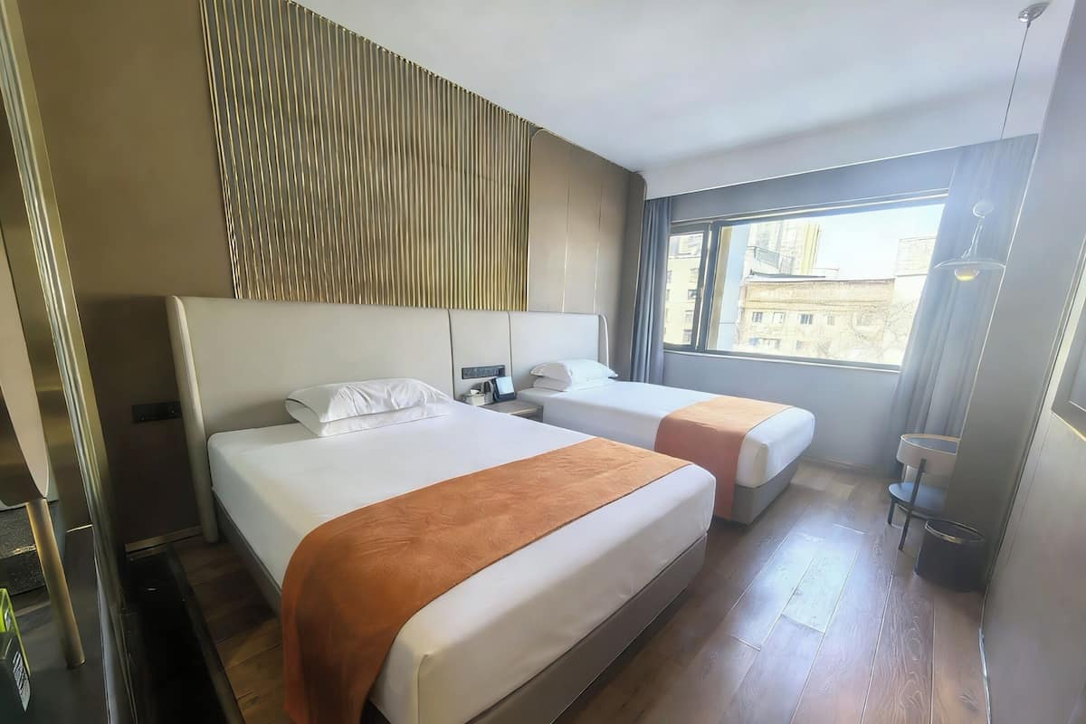 Habitación de hotel con dos camas, piso de madera, ventana con vistas a edificios y un diseño moderno.