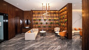 A modern lobby with a sofa, chairs, a coffee table, a reception desk, and a wall with shelves and plants.