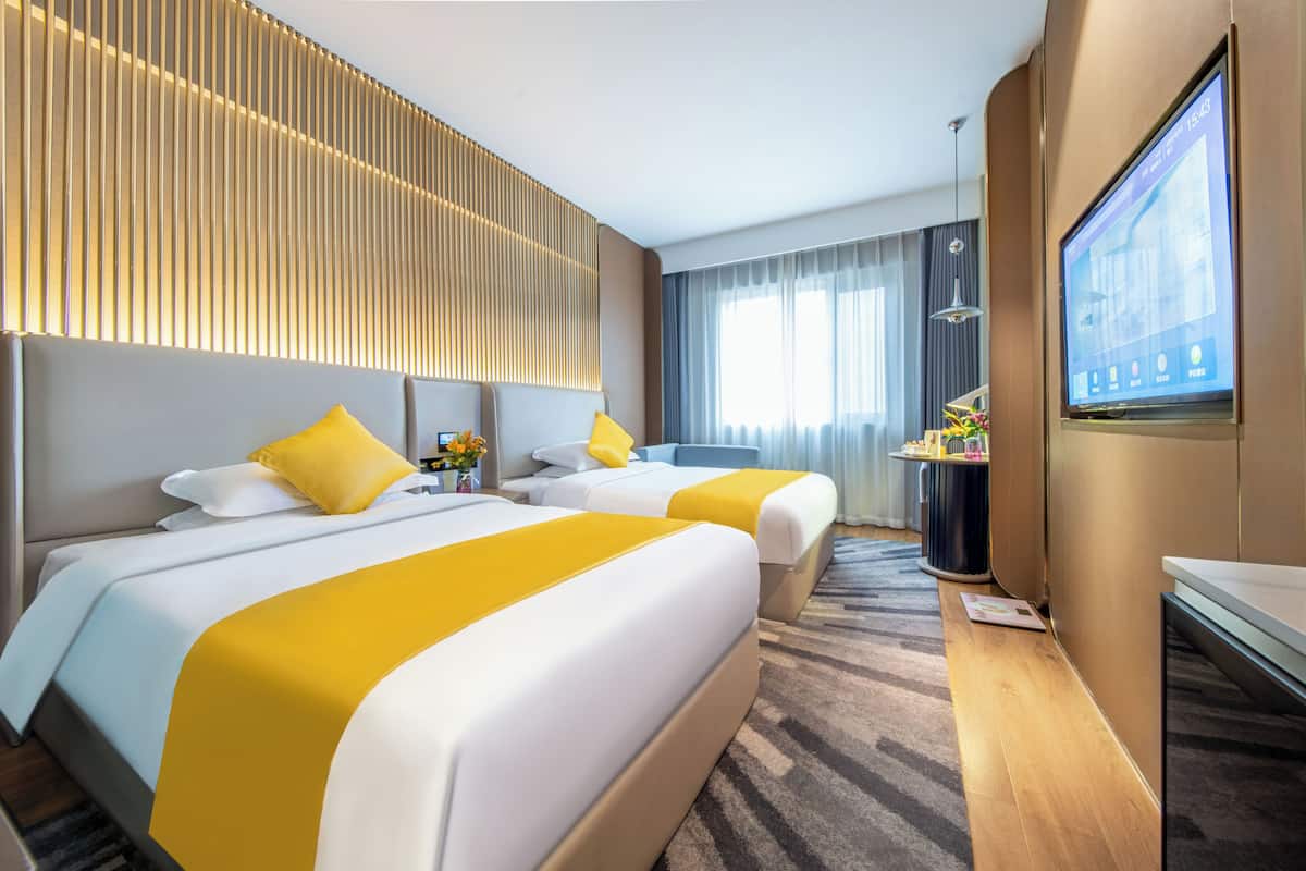 Habitación de hotel con dos camas, televisor, escritorio y ventana con cortinas.