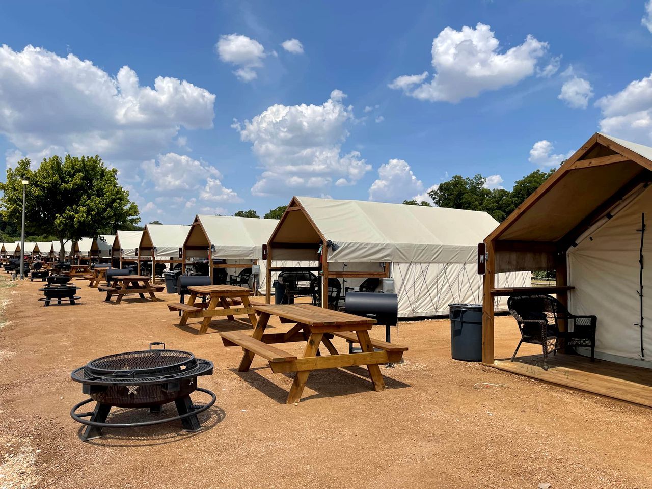 A campsite with multiple tents, picnic tables, and barbecue grills.