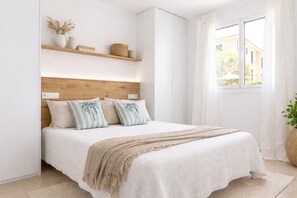 Ein Schlafzimmer mit einem Holzkopfteil, einem Bett mit weißer Bettwäsche, einer beigen Tagesdecke und einem Fenster mit Vorhängen.