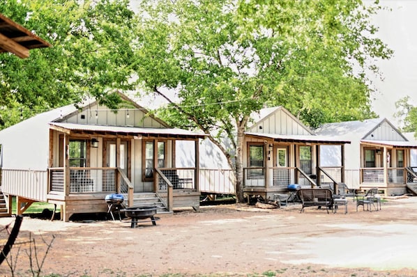 Une rangée de maisons mobiles dotées de terrasses et d’escaliers en bois, chacune ayant un barbecue et un espace salon extérieur.