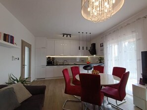 Une cuisine moderne avec des meubles blancs, un coin repas avec des chaises rouges et un lustre.