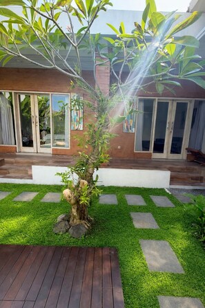 Un jardín con un árbol, un sendero de piedra y una terraza de madera.