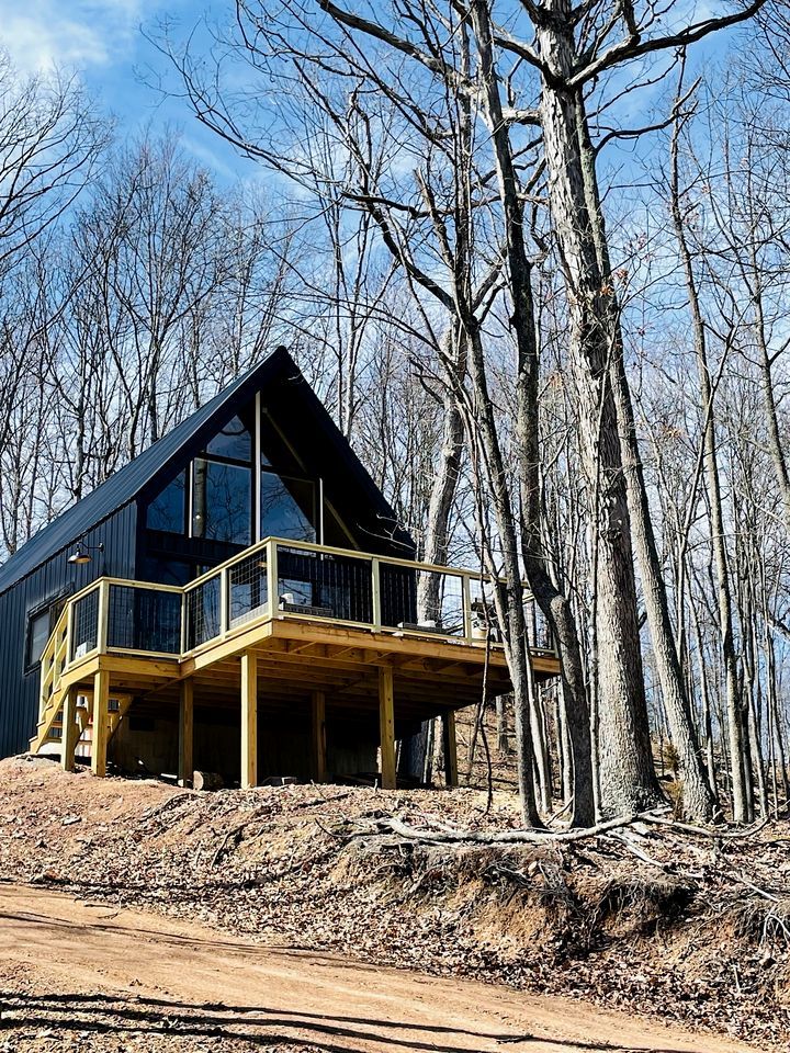 A modern wooden cabin with a balcony, surrounded by trees.