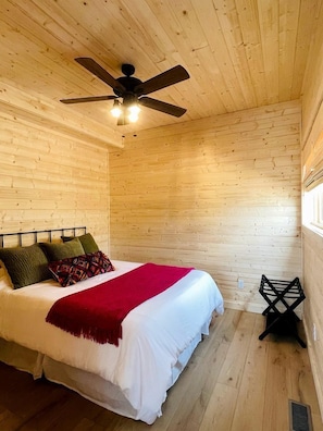 A wooden-paneled room with a bed, a ceiling fan, and a window. - Gorgeous A-Frame Cabin Nestled in the Trees near Lost River, West Virginia (Mathias)