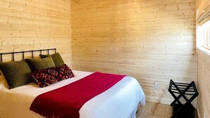Una habitación con paneles de madera, una cama, un ventilador de techo y una ventana.