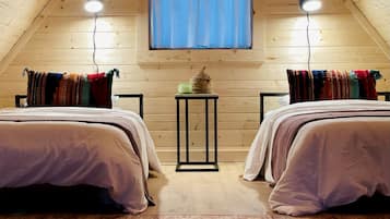 A cozy attic bedroom with two beds, a small table, and a window with curtains.