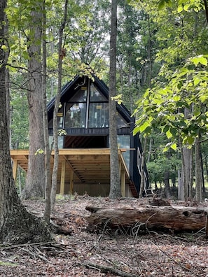 Une cabane dotée d’une terrasse en bois, de grandes fenêtres et donnant sur une forêt.