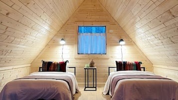 A cozy attic bedroom with two beds, a window with curtains, and a hanging light fixture.