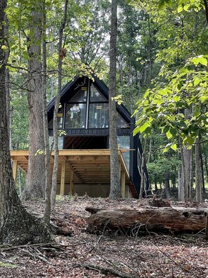 A cabin with a wooden deck, large windows, and a forest backdrop. - Gorgeous A-Frame Cabin Nestled in the Trees near Lost River, West Virginia (Mathias)