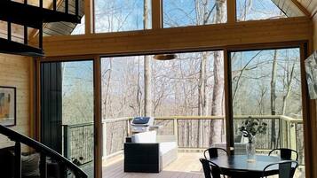 A spacious interior with a high ceiling, large windows, a dining area with chairs, and a staircase.