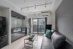 Et moderne køkken med indbygget komfur, et spiseområde med bord og stole, en sofa med pude, og et stort vindue med gardiner.