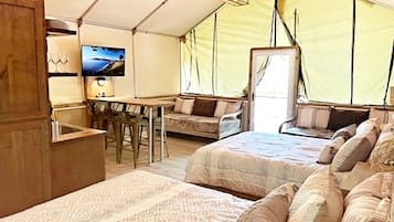A tented accommodation with two beds, a desk, a TV, and a dining area.