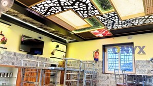 Interior de un restaurante con techo alto, diseño de techo estampado, paredes con azulejos y un extintor colgado en la pared.