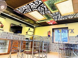 Interior de un restaurante con techo alto, diseño de techo estampado, paredes con azulejos y un extintor colgado en la pared.