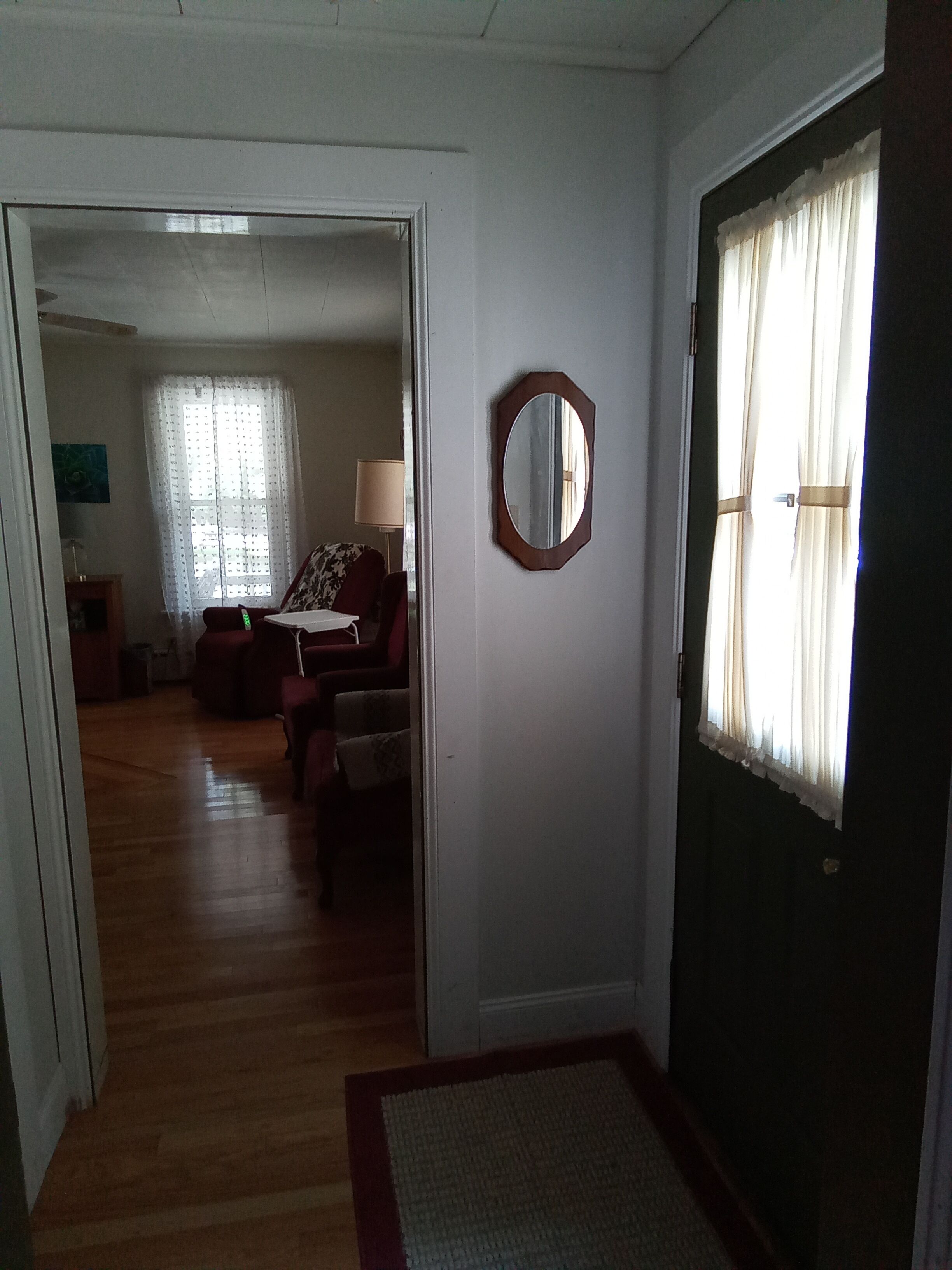 A hallway leading to a living room with a sofa, a lamp, and a mirror on the wall.