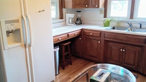 A kitchen with wooden cabinets, a refrigerator, a coffee maker, a sink, and a glass table. - Homestead on Mill St. (Woolrich)