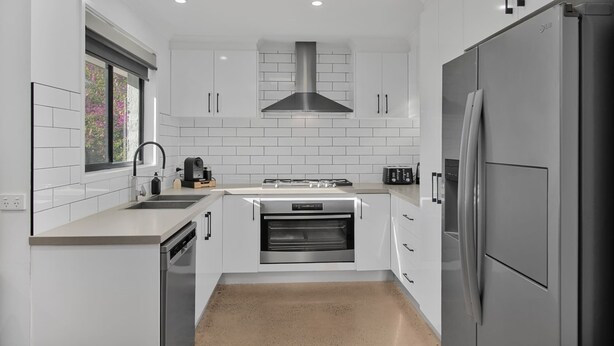 Una cocina moderna con armarios blancos, un refrigerador de acero inoxidable, un horno empotrado y una ventana con vistas a flores rosadas.