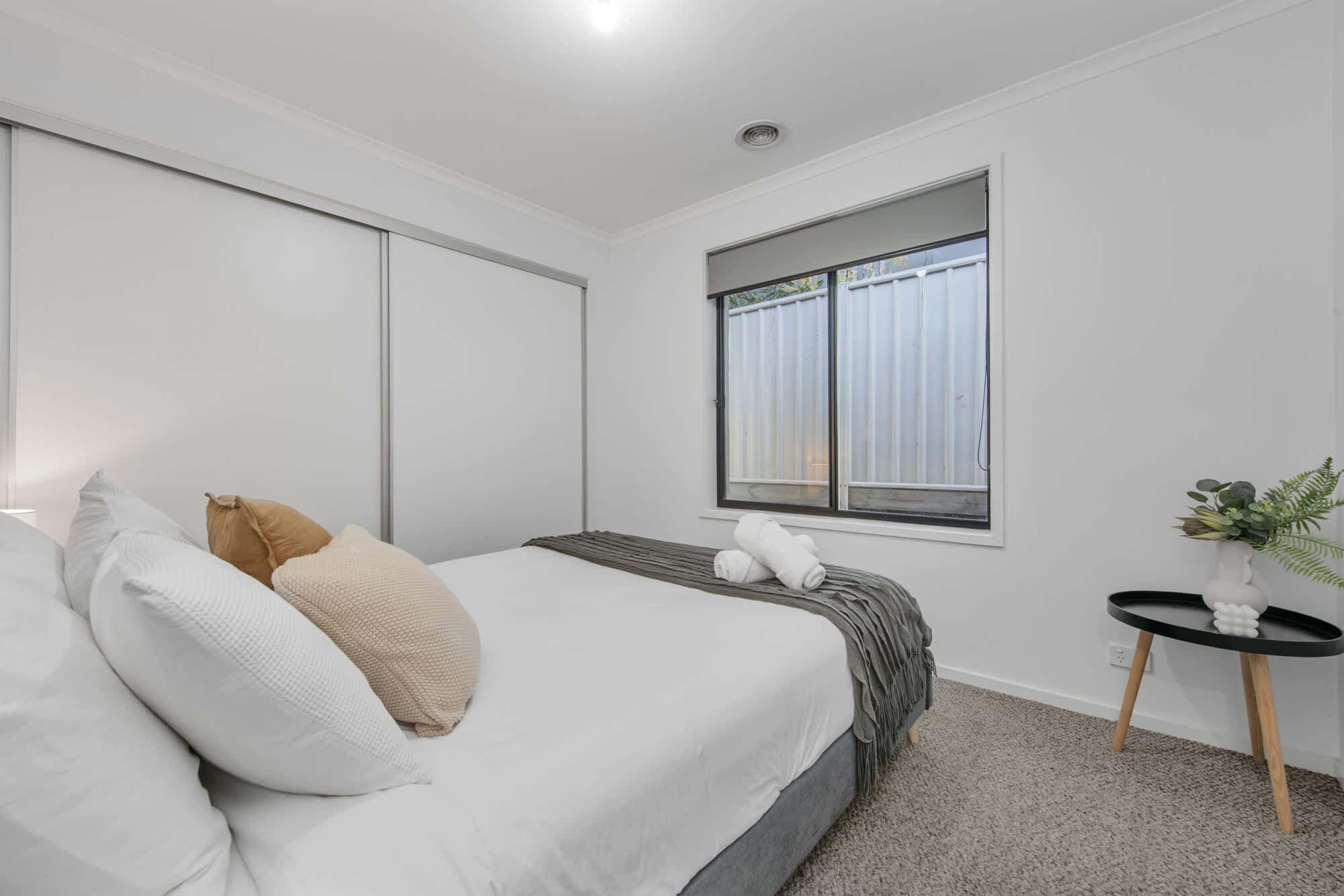Une chambre à coucher avec un lit, des oreillers, une table de chevet, une fenêtre et une plante.