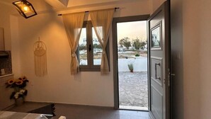 A room with a bed, a window with curtains, a hanging light fixture, and a view of the outside. - Tranquil Guest Room Retreat in Vothonas, Santorini (Vothonas)
