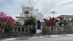 A white building with a stone wall and pink flowers in front. - Tranquil Guest Room Retreat in Vothonas, Santorini (Vothonas)
