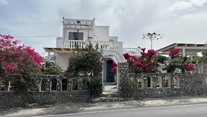 Un bâtiment blanc avec un mur en pierre et des fleurs roses devant.