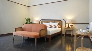 A hotel room with a bed, a sofa, a nightstand with a lamp, and a small table with a tray. - La Villa des Chien (Sattahip)