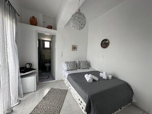 Une chambre à coucher avec un lit, une table de chevet, un luminaire suspendu, un tapis à motifs et une vue sur la salle de bain.