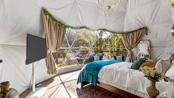 Een tentachtige kamer met een bed, gordijnen, een kroonluchter en een televisie.