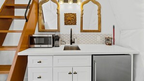 A compact kitchen with a microwave, sink, and cabinet, a wooden staircase, and decorative wall mirrors. - Beautiful Lofted Dome with Cozy Deck and Charming Design in Elgin, Texas (Elgin)