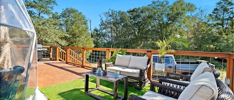 A covered outdoor area with a wooden deck, a wicker sofa, a table with candles, and a vehicle in the background.