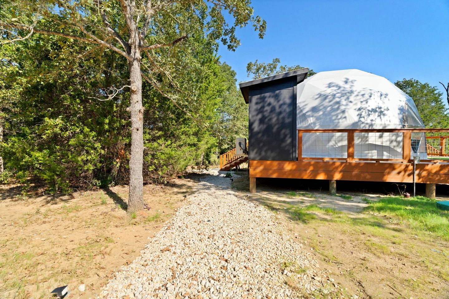 Eine moderne Hütte mit einer großen, kuppelförmigen Struktur, umgeben von Bäumen und einem Kiesweg.